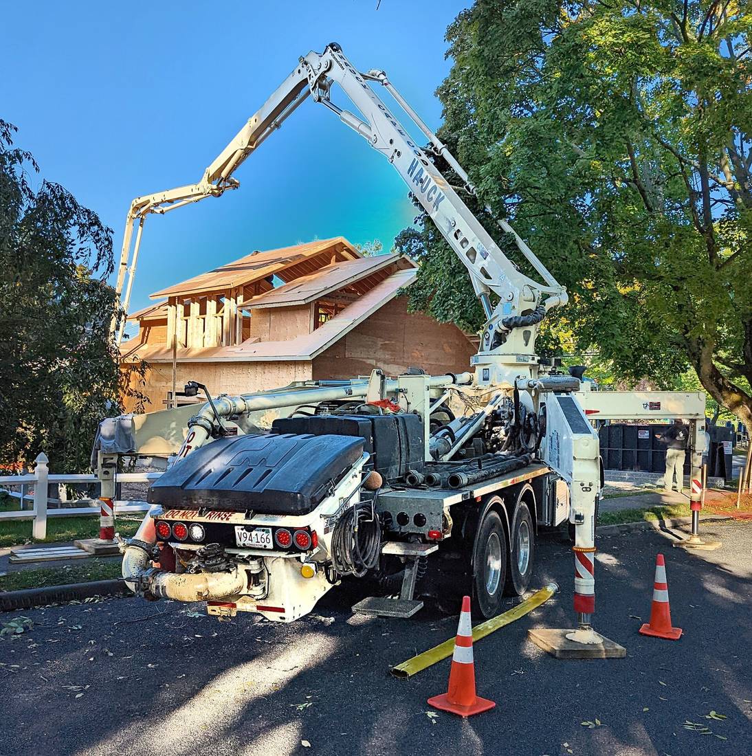 Concrete boom pump truck extended over a residential job site behind safety cones